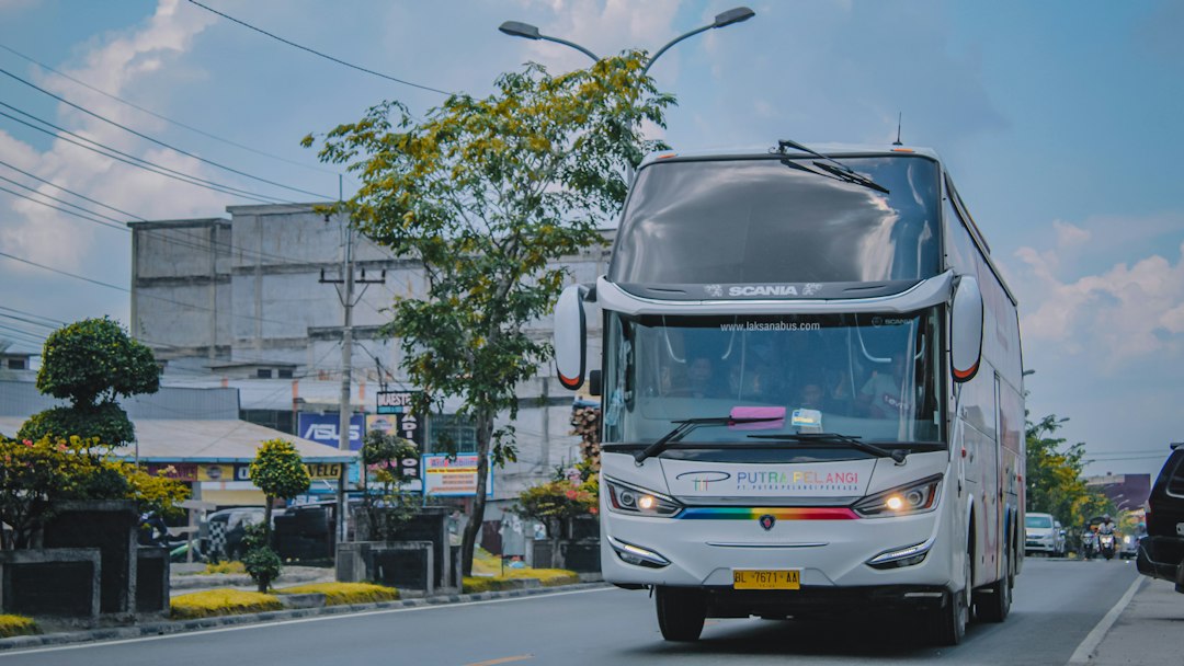 Bus penumpang putih hitam melaju di jalan raya pada siang hari